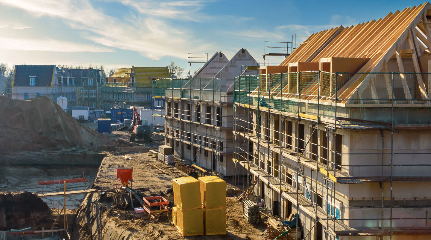 Chantier de construction d'immeubles résidentiels neufs avec structure béton apparente, grue et ouvriers au travail, programme éligible au financement PTZ, zone périurbaine française